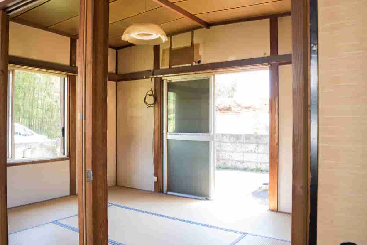 荷物が片付いた後の空き家の和室。畳の部屋に光が差し込み、窓の外には竹林が見える。